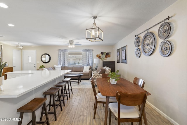 dining room with ceiling fan with notable chandelier, light wood-type flooring, and a textured ceiling