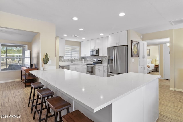 kitchen with appliances with stainless steel finishes, light wood-type flooring, kitchen peninsula, a breakfast bar, and white cabinets