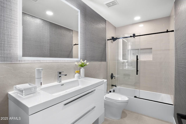 full bathroom featuring toilet, combined bath / shower with glass door, tile walls, vanity, and tile patterned flooring