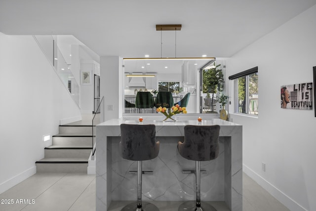 kitchen featuring light stone countertops, pendant lighting, white cabinets, and a kitchen breakfast bar