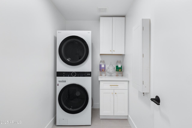 clothes washing area featuring light tile patterned flooring, cabinets, and stacked washer / dryer