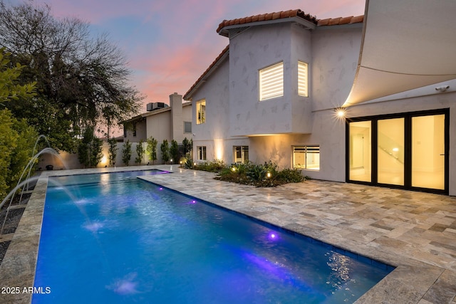 pool at dusk with pool water feature and a patio area