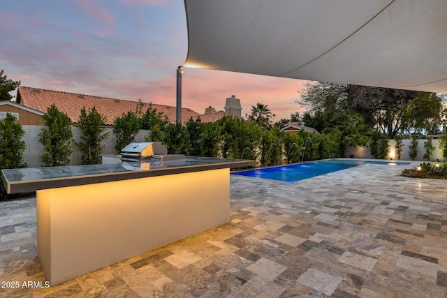 pool at dusk featuring pool water feature, area for grilling, a grill, and a patio