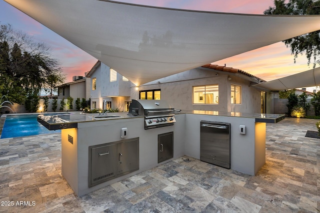 patio terrace at dusk with a grill, pool water feature, area for grilling, and sink