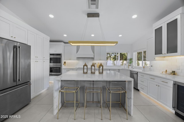 kitchen with a kitchen bar, white cabinetry, a center island, custom range hood, and stainless steel appliances