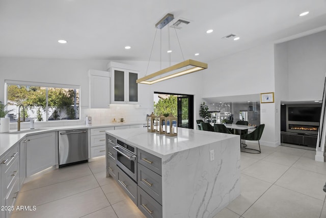 kitchen with sink, appliances with stainless steel finishes, white cabinetry, a kitchen island, and decorative light fixtures