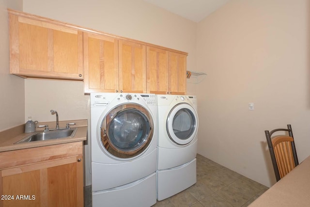 clothes washing area featuring washer and clothes dryer, sink, light tile floors, and cabinets