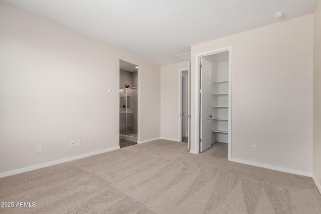 unfurnished bedroom featuring connected bathroom, a spacious closet, light colored carpet, and a closet