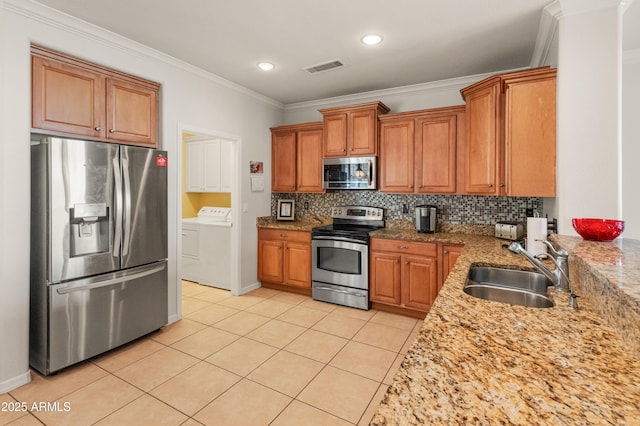 kitchen with light stone counters, sink, washing machine and clothes dryer, and appliances with stainless steel finishes