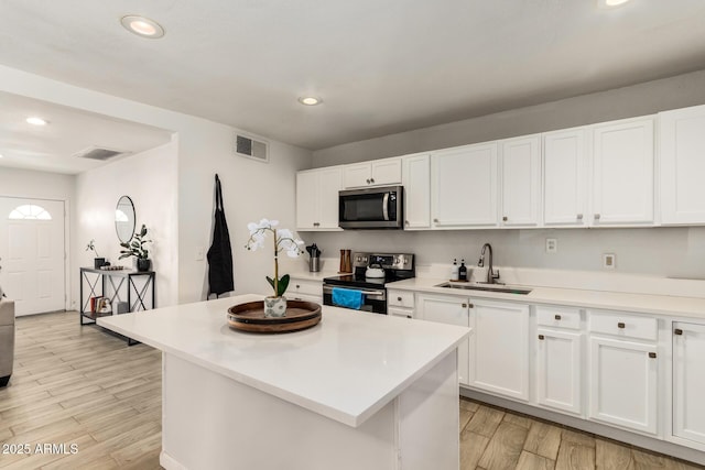 kitchen with sink, white cabinetry, a center island, appliances with stainless steel finishes, and light hardwood / wood-style floors