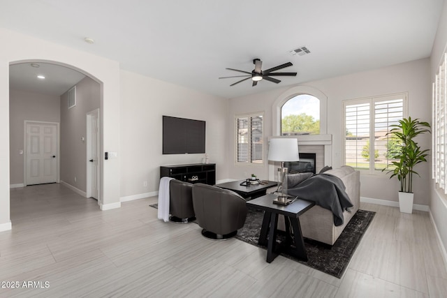 living room with a ceiling fan, baseboards, a glass covered fireplace, and visible vents