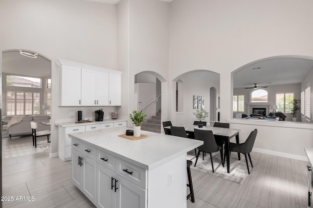 kitchen with a breakfast bar area, white cabinets, a towering ceiling, ceiling fan, and a kitchen island