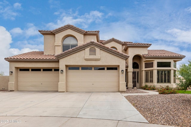 mediterranean / spanish house with an attached garage, concrete driveway, stucco siding, and a tiled roof