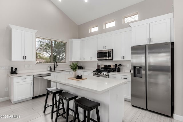 kitchen featuring a sink, a kitchen breakfast bar, high vaulted ceiling, stainless steel appliances, and white cabinets