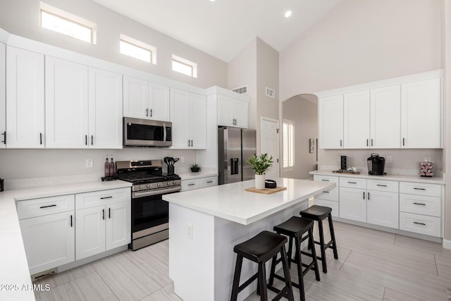 kitchen featuring high vaulted ceiling, a kitchen bar, a center island, arched walkways, and appliances with stainless steel finishes