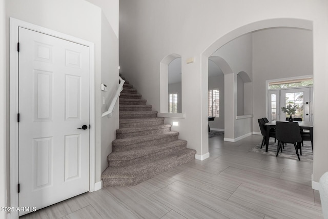 staircase featuring a high ceiling, baseboards, and arched walkways