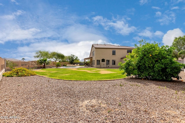 rear view of house with a yard, fence, stucco siding, and a tiled roof