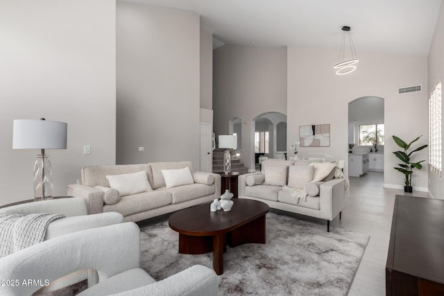 living area with visible vents, baseboards, arched walkways, and high vaulted ceiling