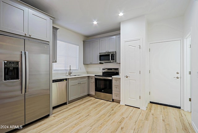 kitchen with gray cabinetry, sink, light hardwood / wood-style flooring, and appliances with stainless steel finishes