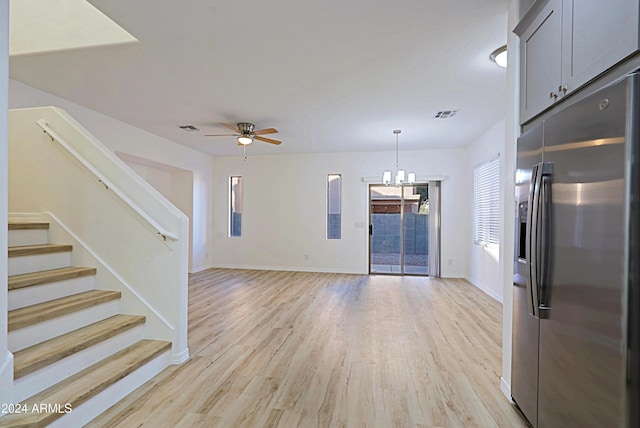 unfurnished living room featuring ceiling fan with notable chandelier and light hardwood / wood-style floors