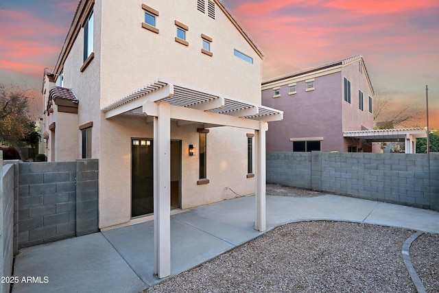 back house at dusk with a pergola and a patio area