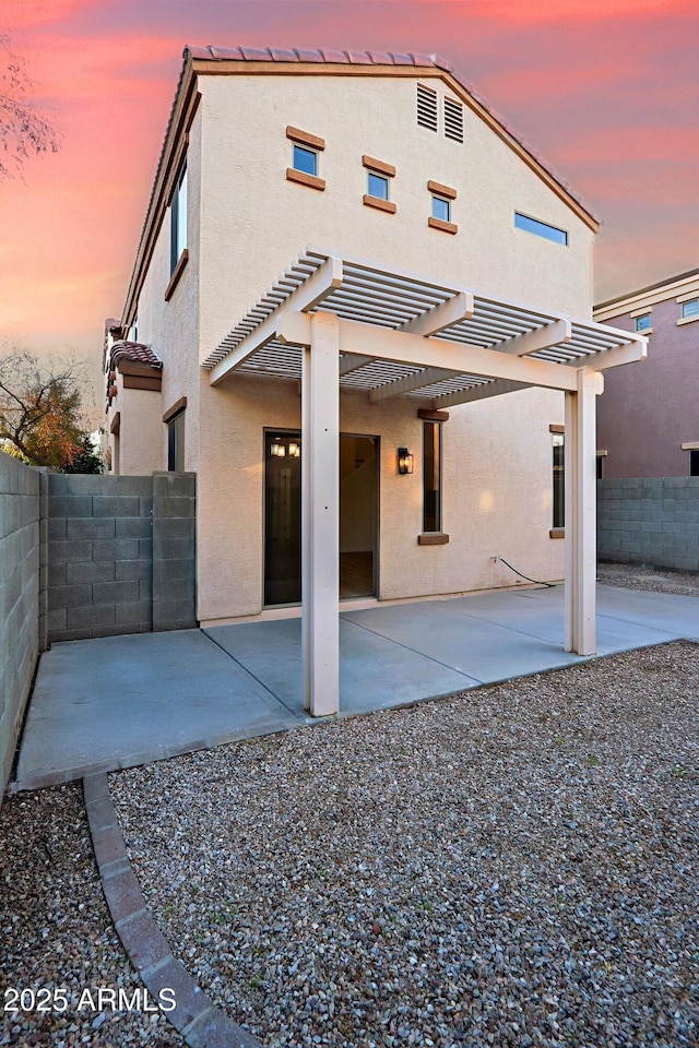 back house at dusk featuring a pergola and a patio