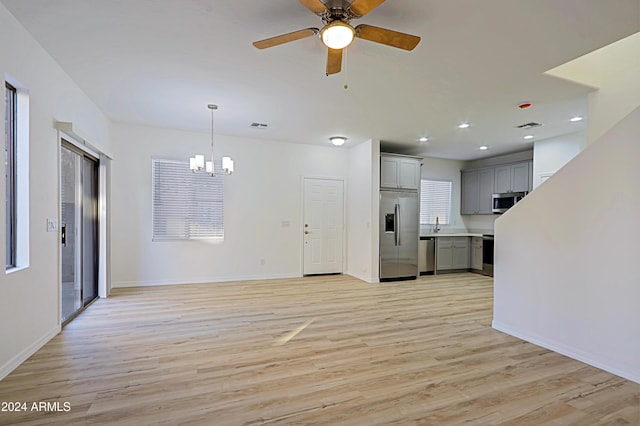 unfurnished living room with ceiling fan with notable chandelier and light hardwood / wood-style flooring