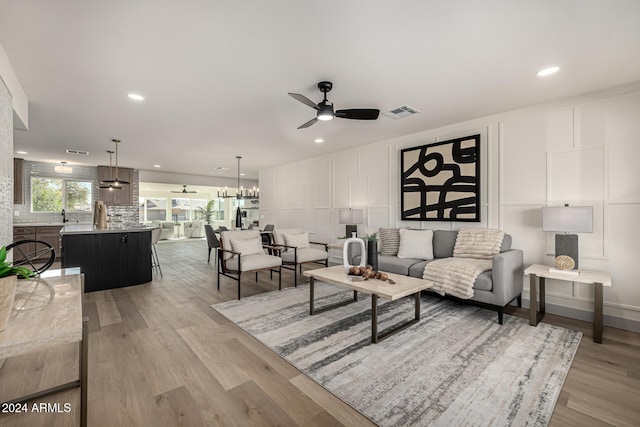 living room with ceiling fan with notable chandelier, light hardwood / wood-style floors, and sink