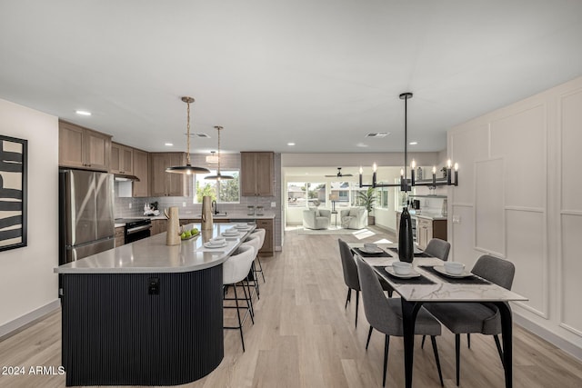 kitchen with hanging light fixtures, black range with electric cooktop, a large island, light hardwood / wood-style floors, and stainless steel refrigerator