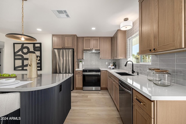 kitchen featuring appliances with stainless steel finishes, backsplash, sink, decorative light fixtures, and light hardwood / wood-style floors