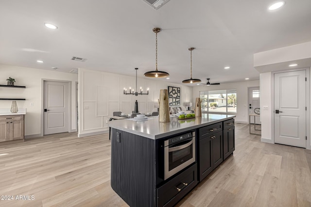 kitchen with ceiling fan with notable chandelier, a kitchen island with sink, pendant lighting, light hardwood / wood-style flooring, and oven