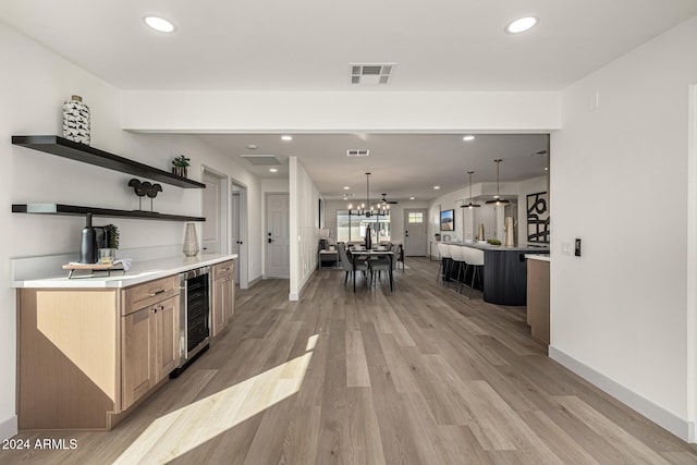 kitchen with light brown cabinetry, a spacious island, light hardwood / wood-style floors, wine cooler, and hanging light fixtures