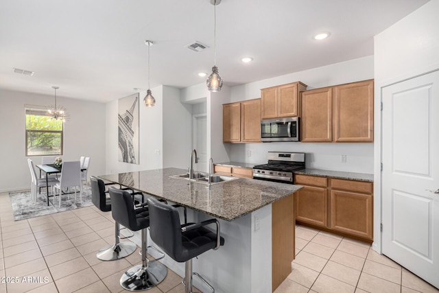 kitchen featuring appliances with stainless steel finishes, brown cabinets, a sink, light tile patterned floors, and dark stone countertops