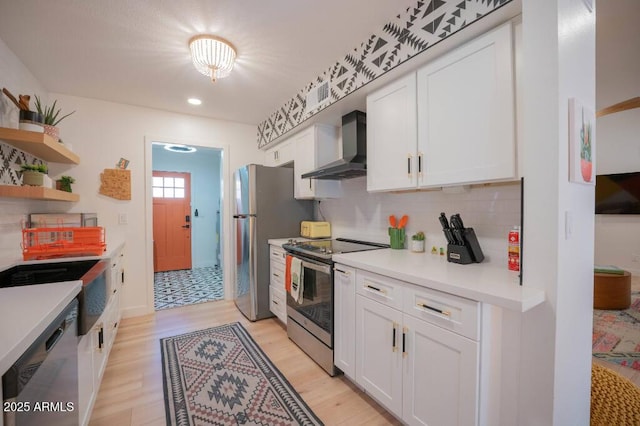 kitchen with white cabinets, appliances with stainless steel finishes, wall chimney range hood, backsplash, and light hardwood / wood-style flooring