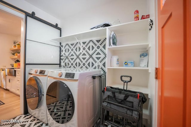 clothes washing area featuring sink, a barn door, washing machine and dryer, and wood-type flooring