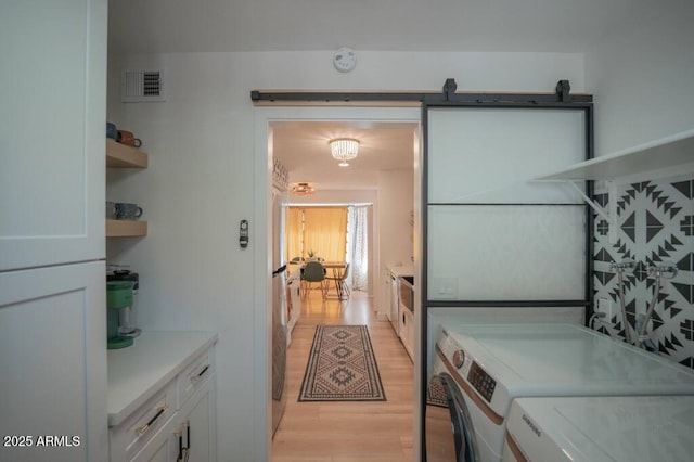 kitchen featuring light wood-type flooring, white cabinetry, a barn door, and independent washer and dryer