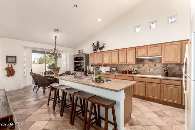 kitchen with decorative backsplash, sink, decorative light fixtures, an inviting chandelier, and a center island with sink