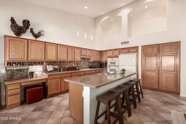 kitchen with sink, a high ceiling, tasteful backsplash, an island with sink, and white appliances