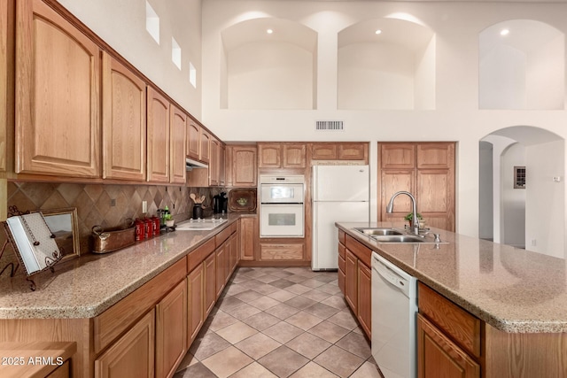 kitchen featuring light stone countertops, sink, a high ceiling, white appliances, and light tile patterned floors