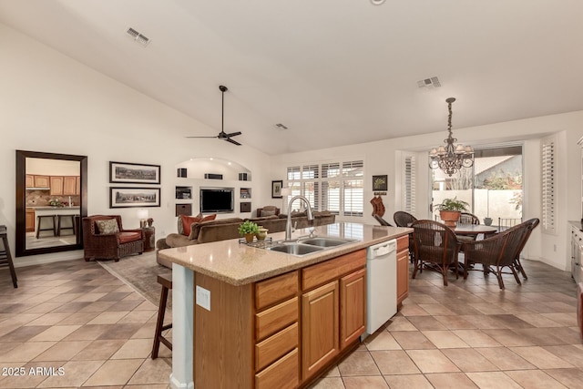 kitchen with light stone counters, ceiling fan with notable chandelier, white dishwasher, pendant lighting, and a center island with sink