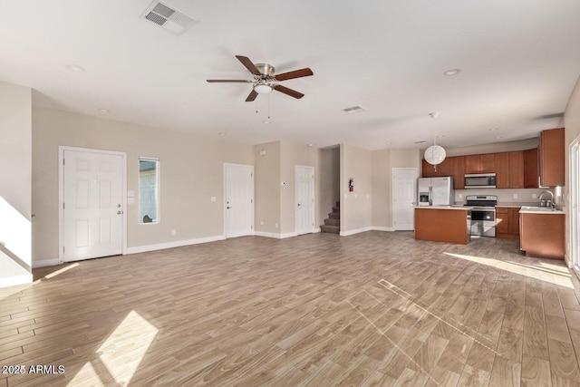 unfurnished living room with a sink, visible vents, baseboards, stairs, and light wood-type flooring