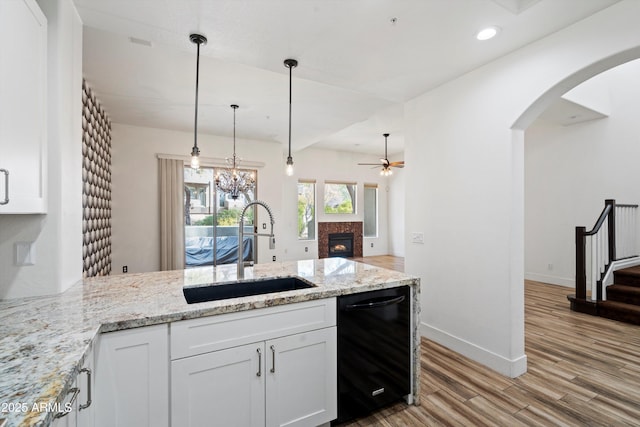 kitchen with a sink, ceiling fan with notable chandelier, a peninsula, black dishwasher, and light wood-style flooring