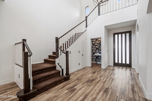 foyer entrance with baseboards, a high ceiling, stairs, and wood finished floors