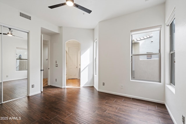unfurnished bedroom featuring arched walkways, baseboards, visible vents, and wood finished floors