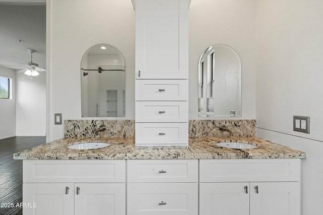 full bathroom featuring double vanity, ceiling fan, a shower stall, and a sink