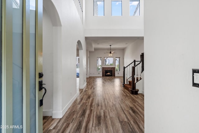 foyer with ceiling fan, a warm lit fireplace, stairway, dark wood-type flooring, and arched walkways