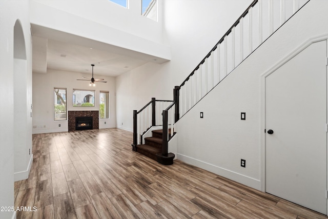 foyer featuring baseboards, a ceiling fan, a warm lit fireplace, and wood finished floors