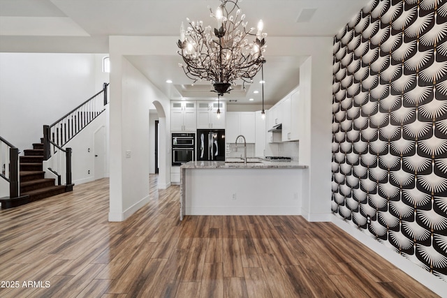 kitchen featuring a sink, arched walkways, a peninsula, wood finished floors, and black appliances