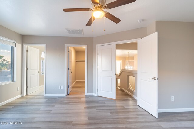 unfurnished bedroom with connected bathroom, a spacious closet, light hardwood / wood-style flooring, a closet, and ceiling fan with notable chandelier