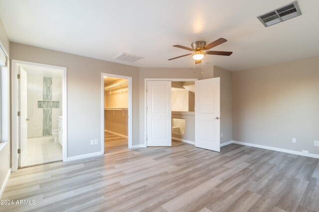 unfurnished bedroom featuring ensuite bath, ceiling fan, light hardwood / wood-style flooring, and a spacious closet